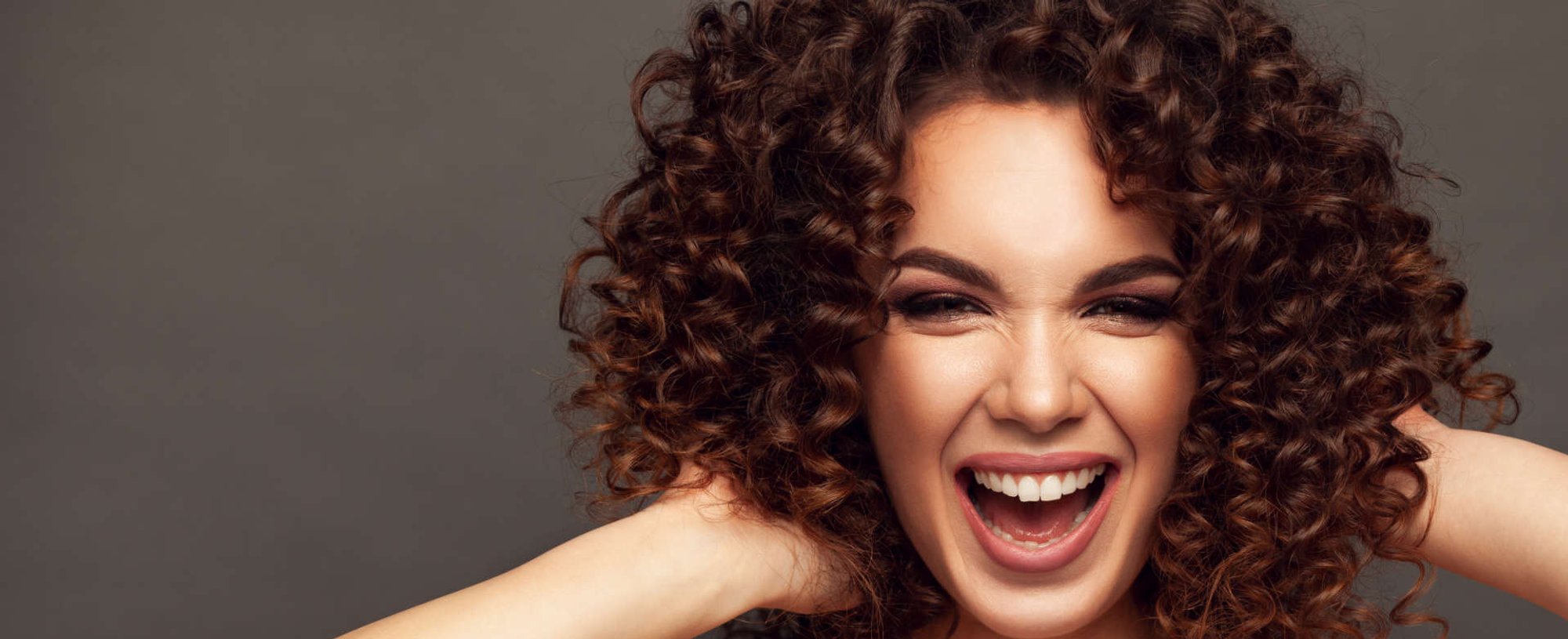 Modelo branca sorrindo com as mãos em seus cabelos cacheados