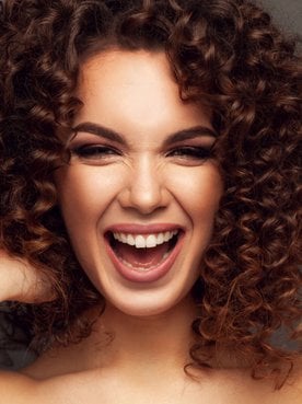Modelo branca sorrindo com as mãos em seus cabelos cacheados