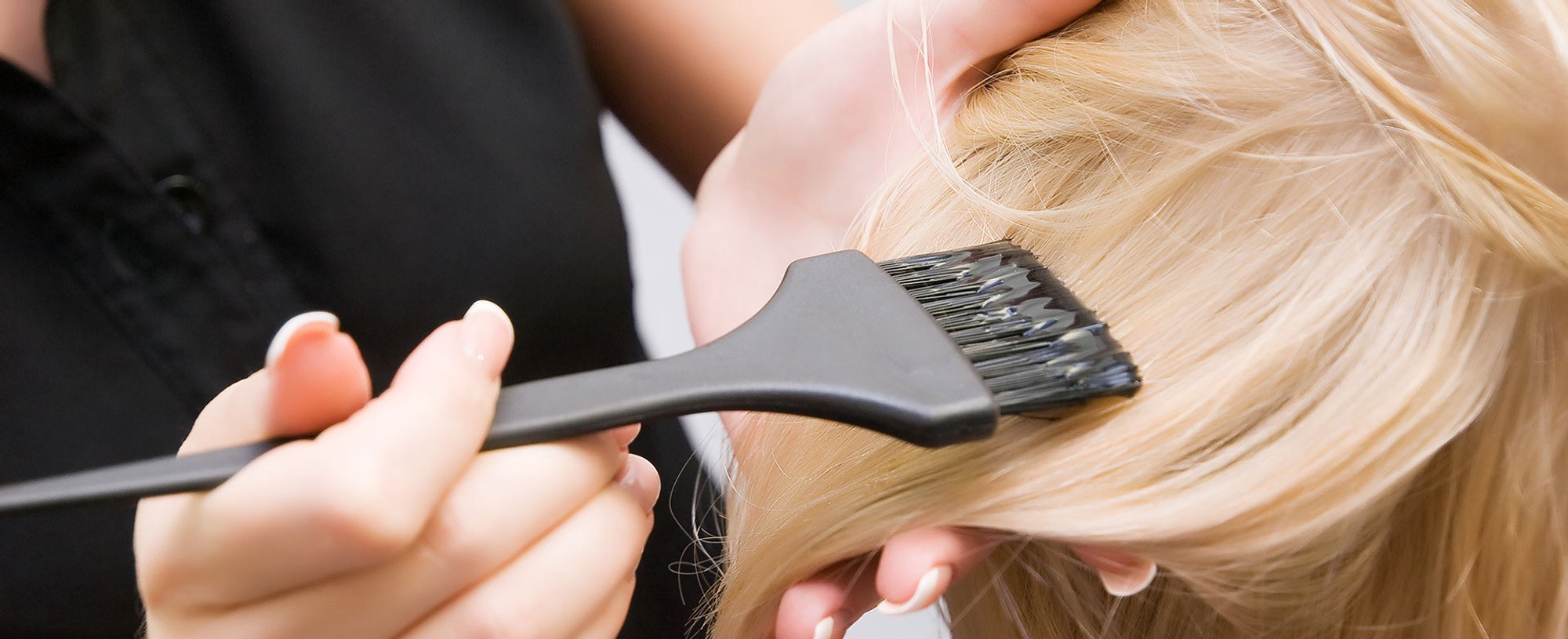 Profissional passando produto em cabelo loiro