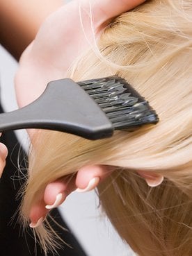 Profissional passando produto em cabelo loiro