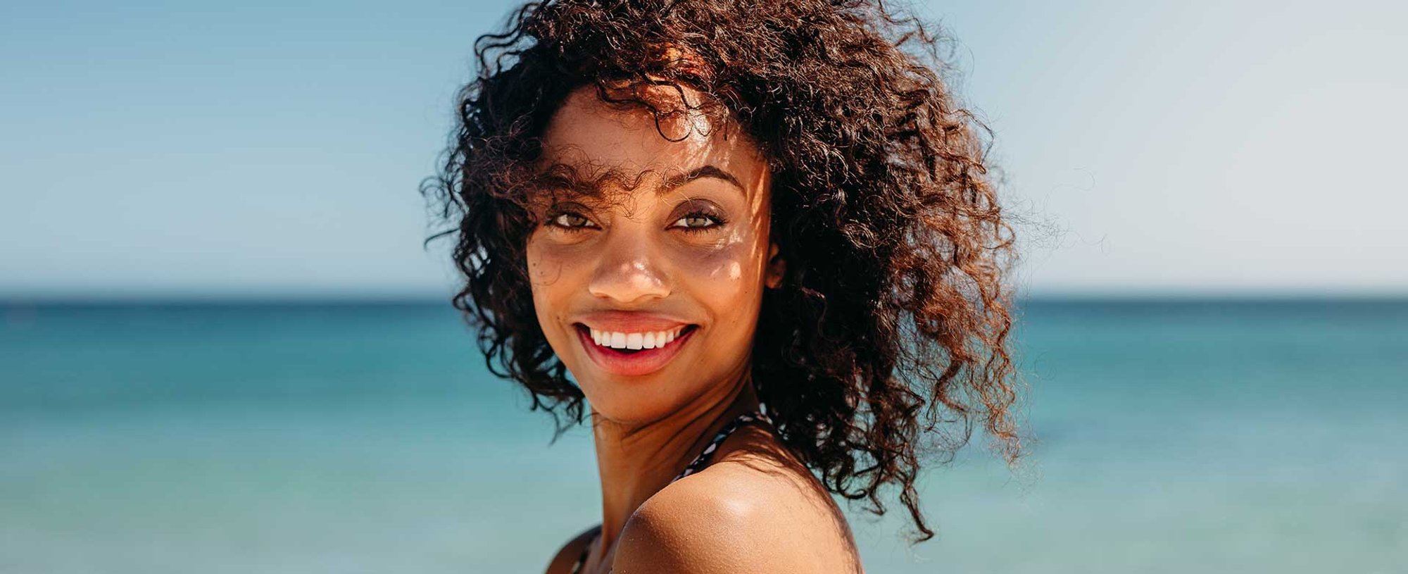 Modelo morena com cabelo cacheado sorrindo na praia