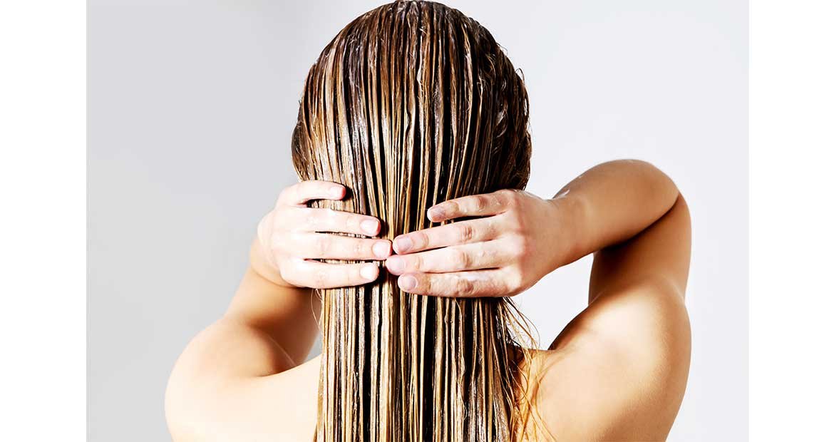 Modelo passando produto em seu cabelo de costas