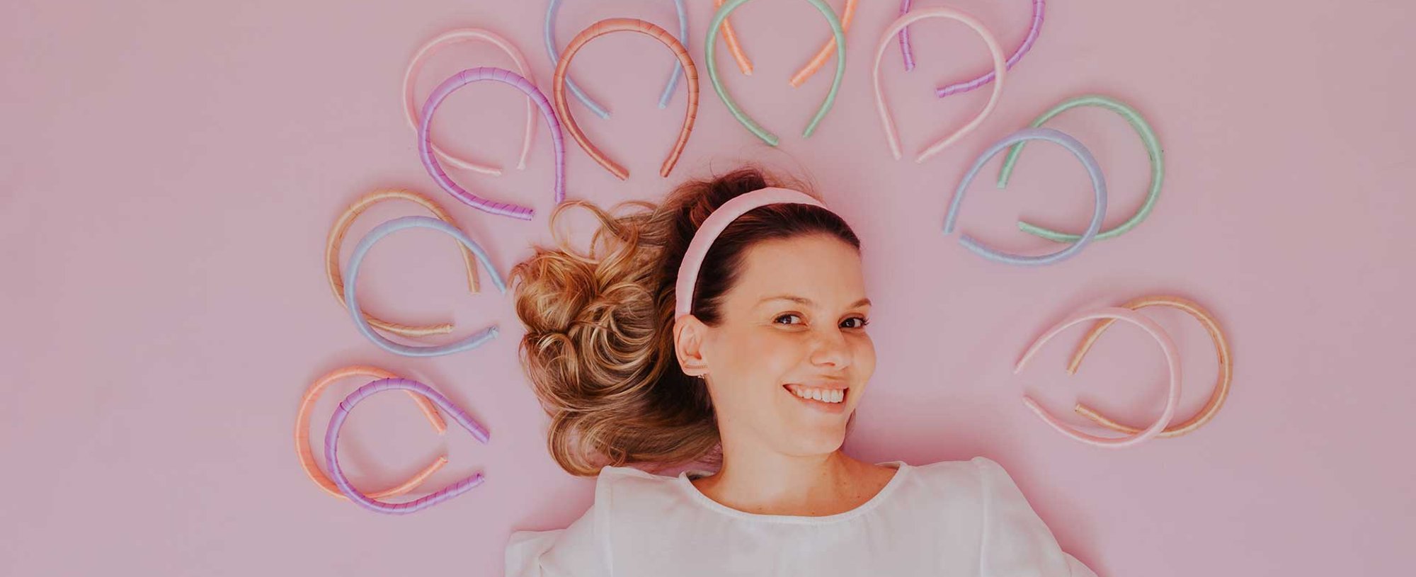 Modelo Com Cabelo Loiro Envolto Por Varias Tiaras Com Fundo Rosa