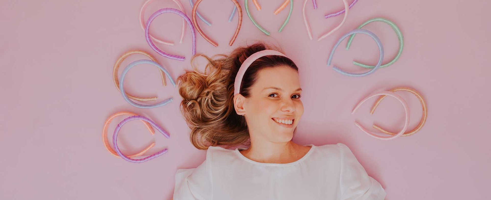 Modelo Com Cabelo Loiro Envolto Por Varias Tiaras Com Fundo Rosa