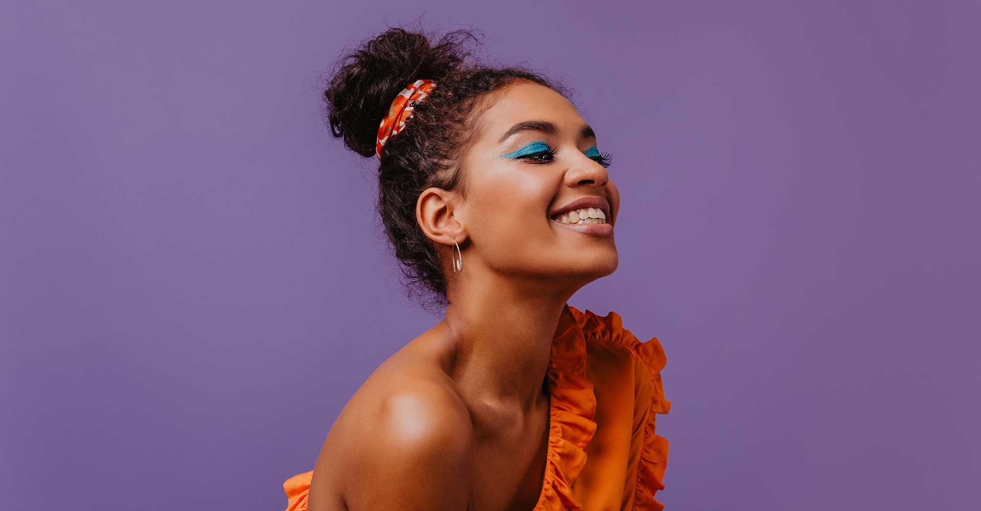 Modelo morena sorrindo com os olhos fechados com cabelo preso com um leno