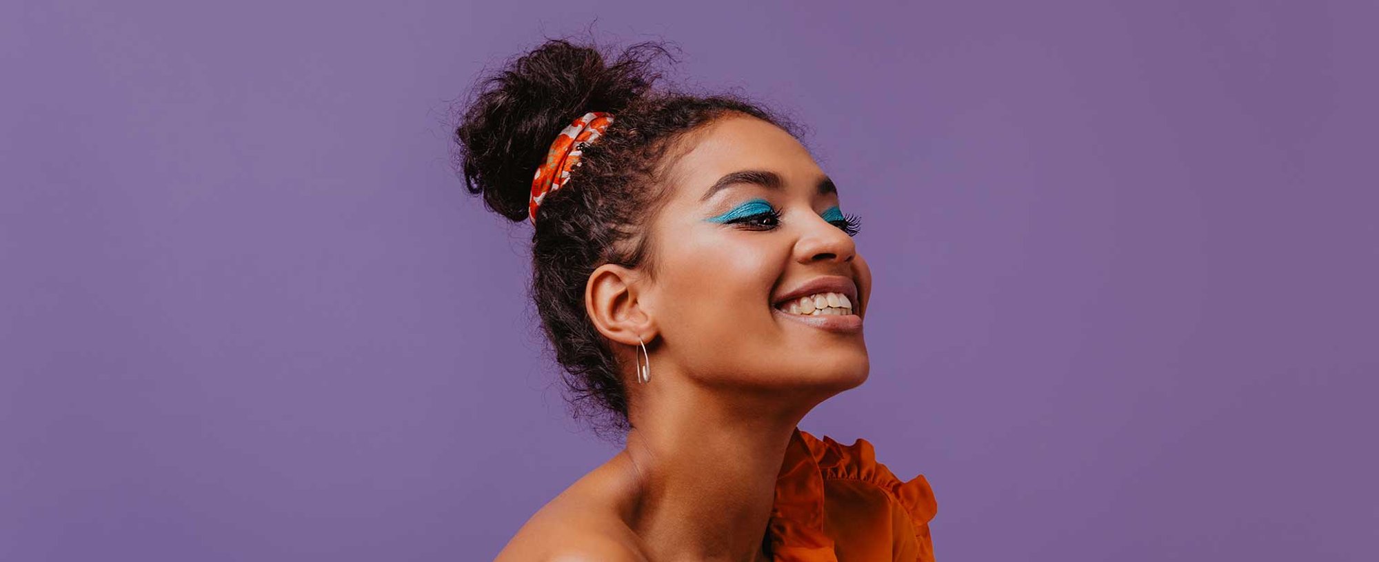 Modelo morena sorrindo com os olhos fechados com cabelo preso com um leno