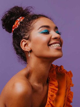 Modelo morena sorrindo com os olhos fechados com cabelo preso com um leno