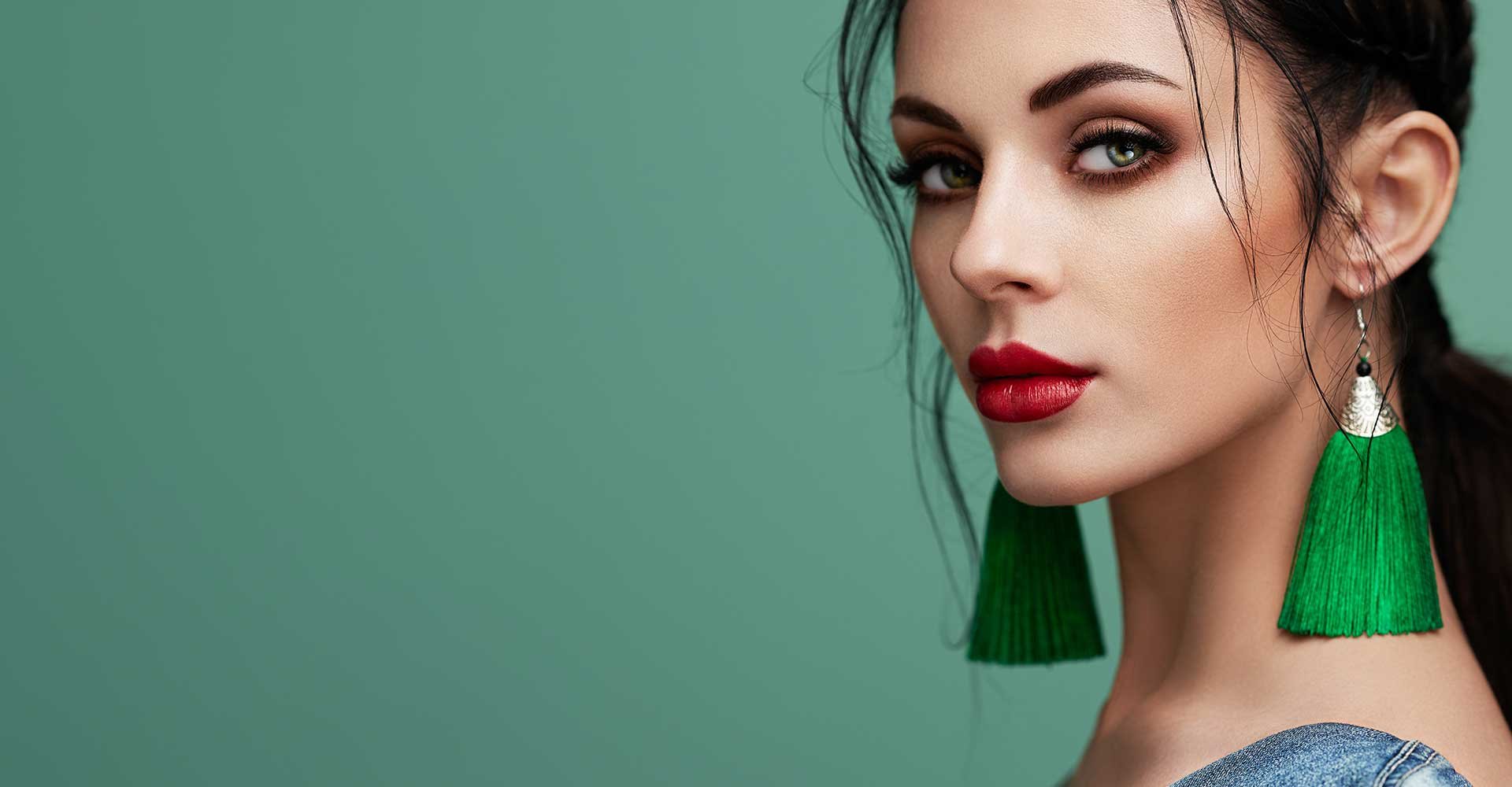 Imagem de uma mulher branca, olhos verdes, batom vermelho e brincos verdes