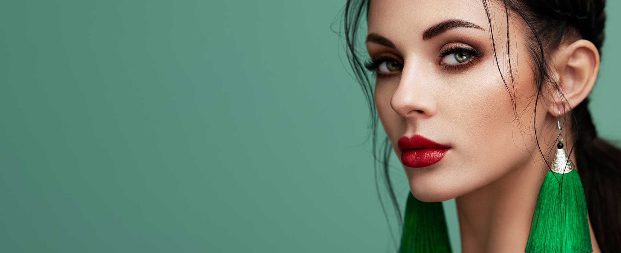 Imagem de uma mulher branca, olhos verdes, batom vermelho e brincos verdes