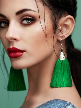 Imagem de uma mulher branca, olhos verdes, batom vermelho e brincos verdes