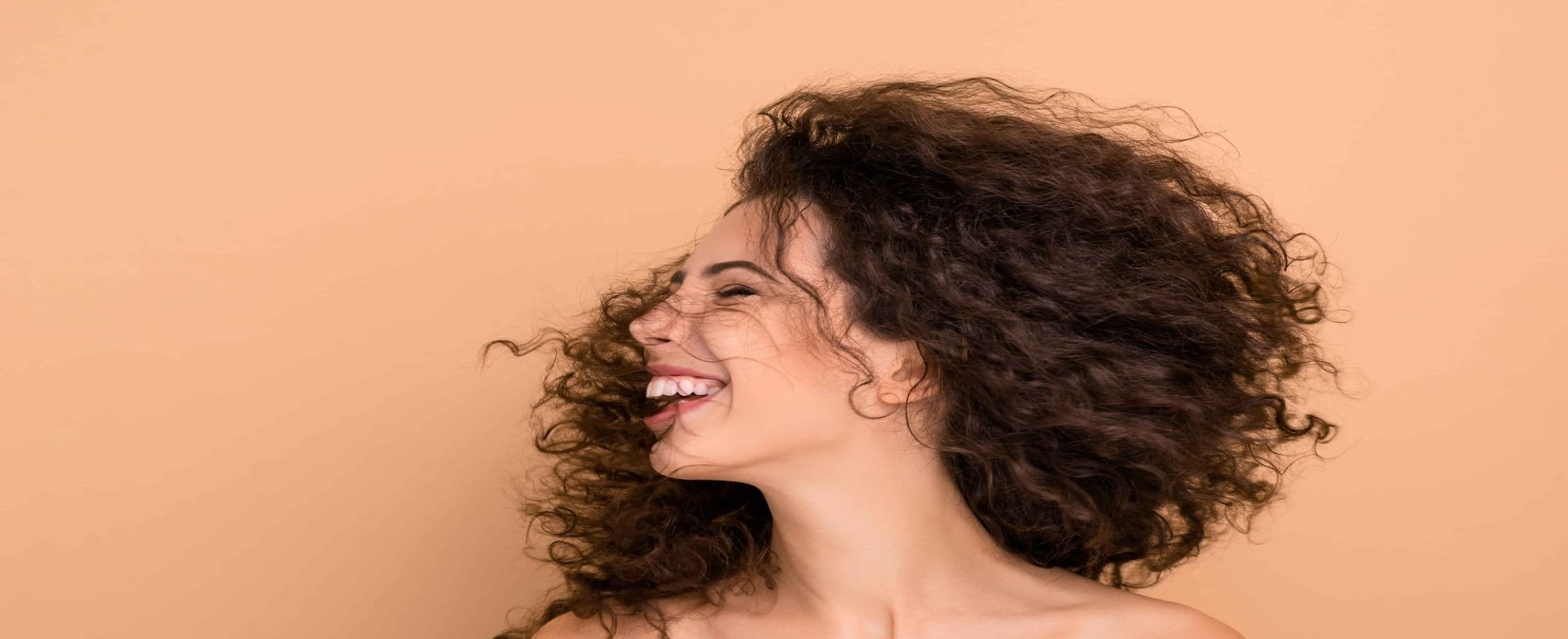 Modelo branca balançando seus cabelos cacheados e sorrindo