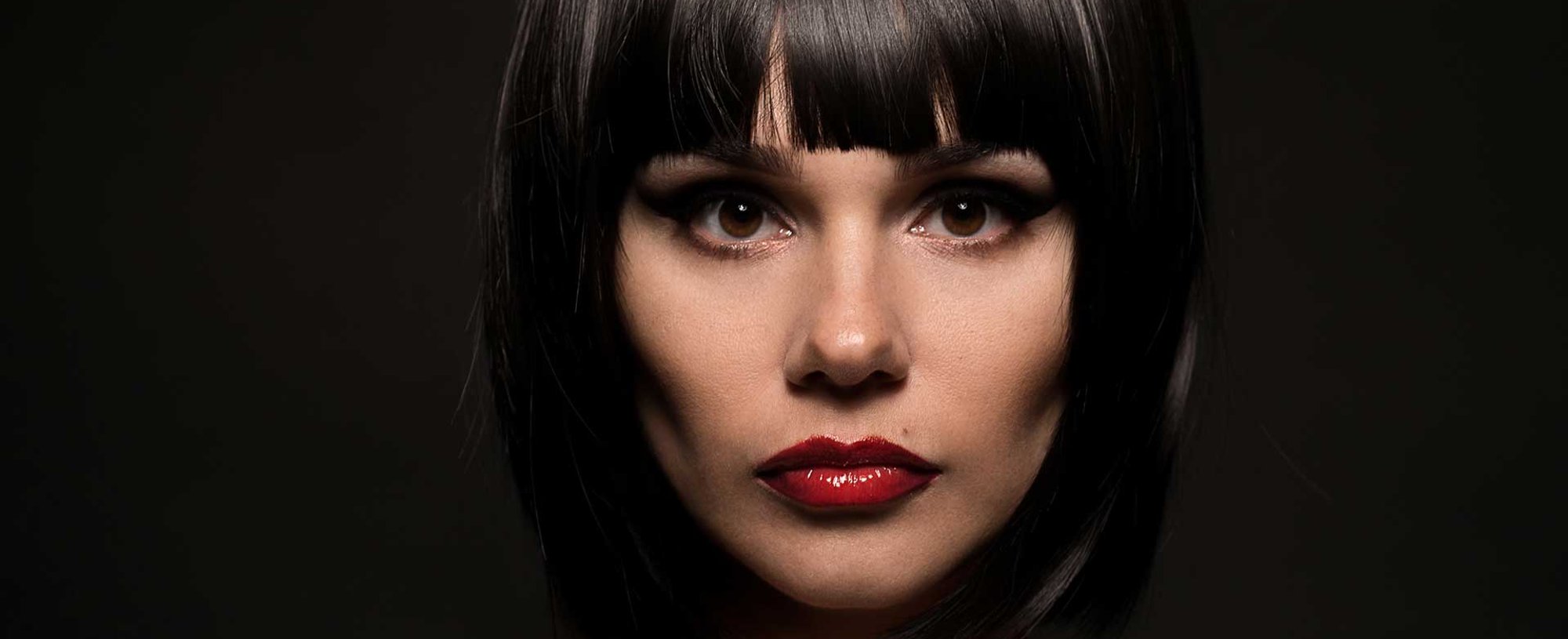 Mulher branca com batom vermelho e cabelo chanel preto com franja