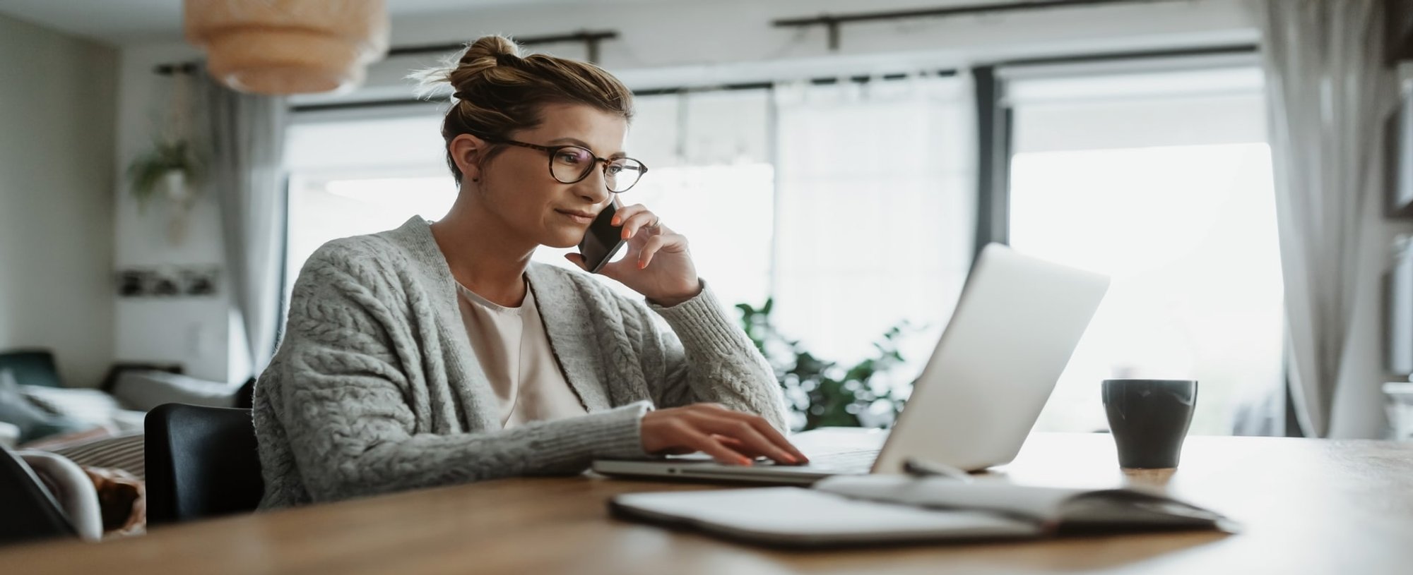 Mulher falando no celular e mexendo no computador no escritório