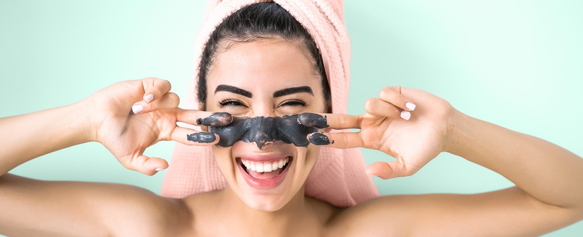 Imagem de mulher com toalha na cabeça e com mascara de argila preta no rosto.