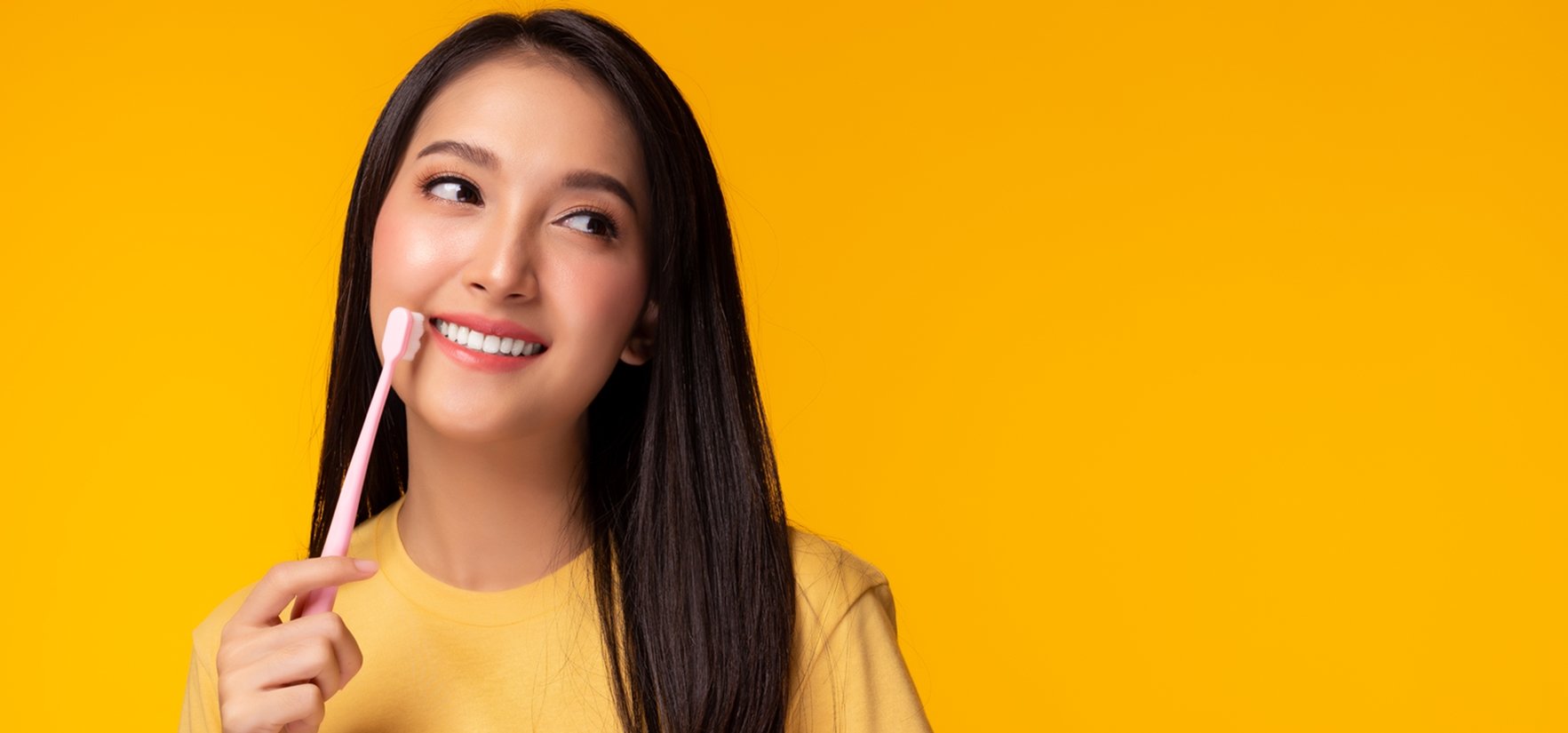 Imagem mostra mulher branca, sorridente com uma escova de dente na mão 