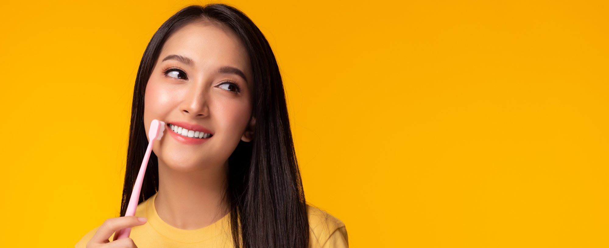 Imagem mostra mulher branca, sorridente com uma escova de dente na mão