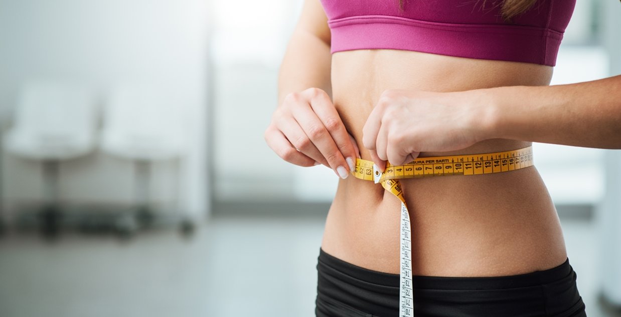 Imagem de modelo branca, com fita medidora em volta de sua barriga.