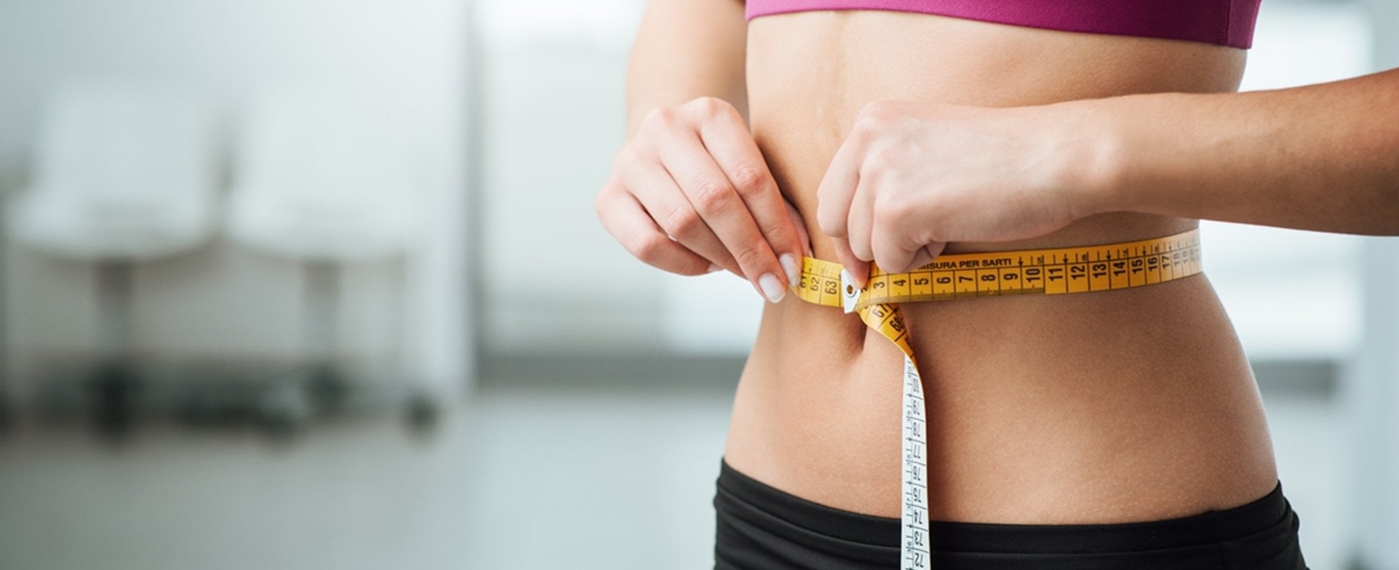 Imagem de uma mulher segurando uma fita medidora em volta de sua barriga.
