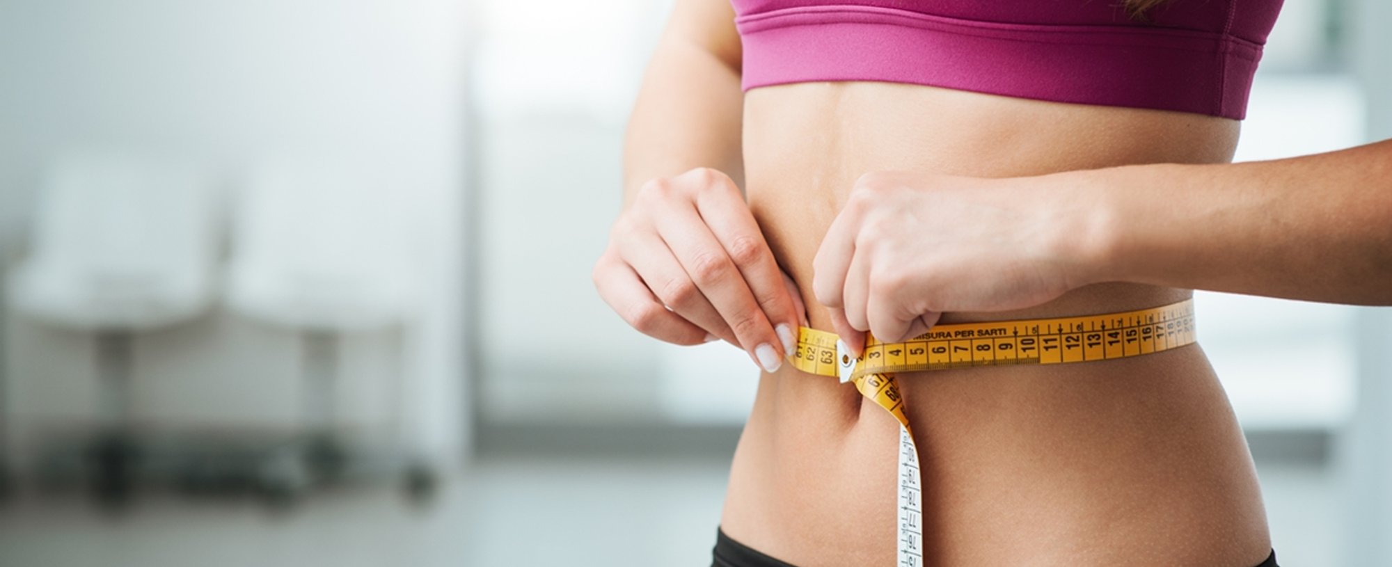 Imagem de modelo branca, com fita medidora em volta de sua barriga.