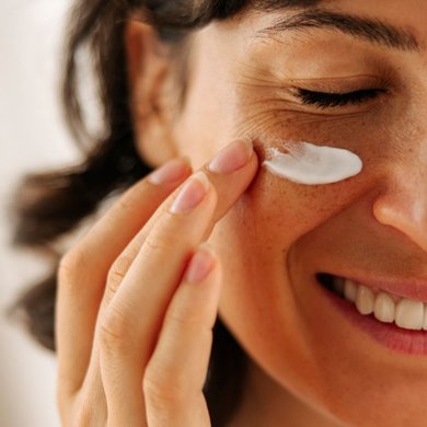 Mulher sorrindo e aplicando protetor solar depois do sérum facial