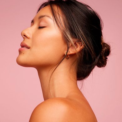 Mulher asiática de olho fechado após aplicar sérum facial
