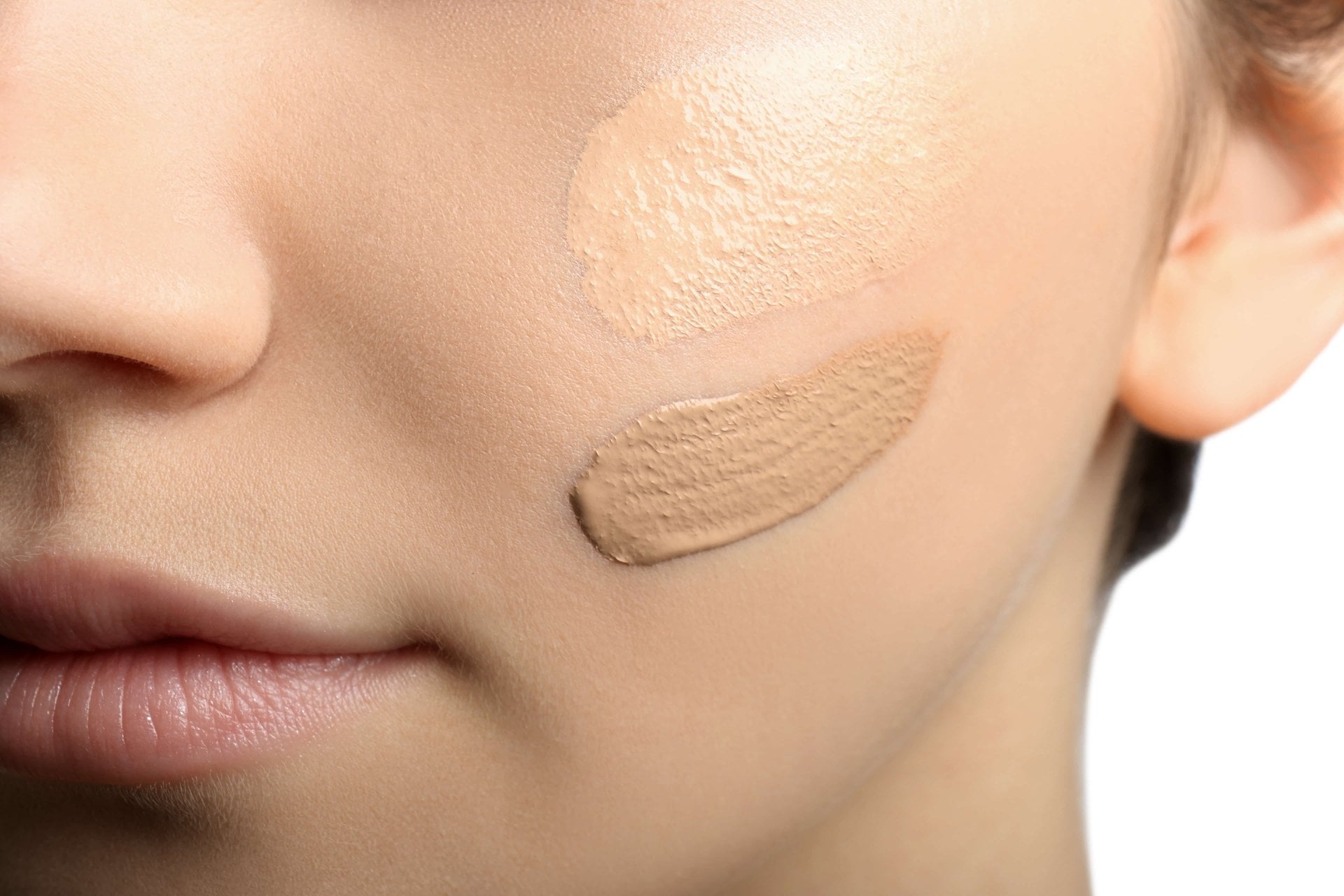 Rosto feminino com duas amostras de protetor facial com cor em tons diferentes aplicadas na bochecha para comparação de cobertura e tonalidade.