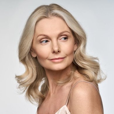 Mulher mais velha com cabelo loiro ondulado olhando para o lado. Após o uso de magic retouch para uniformizar o tom da raiz.