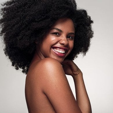 Mulher sorrindo com cabelo preto afro volumoso. Após uso de magic retouch para cobrir os fios brancos.